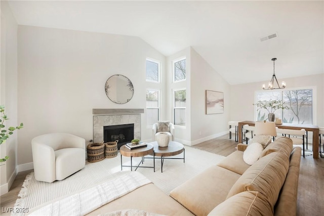 living area with a chandelier, wood finished floors, visible vents, baseboards, and a tiled fireplace