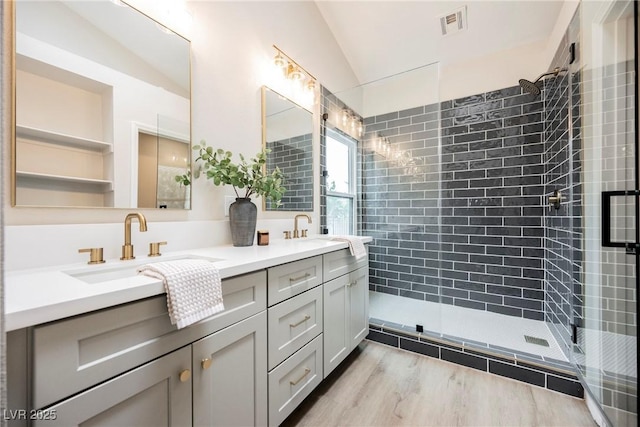 bathroom featuring a tile shower, double vanity, a sink, and visible vents