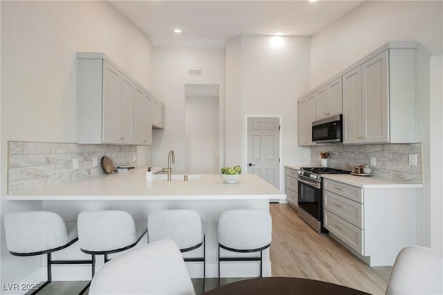 kitchen featuring a breakfast bar, visible vents, a sink, stainless steel gas range, and a peninsula