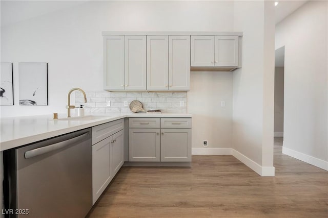 kitchen featuring light wood finished floors, stainless steel dishwasher, backsplash, and a sink