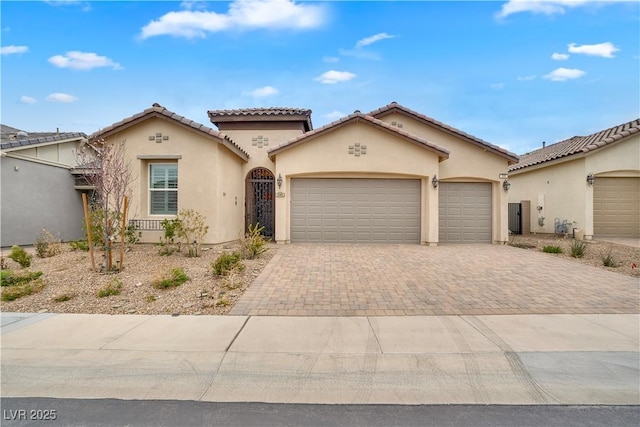 mediterranean / spanish house with decorative driveway, a tiled roof, an attached garage, and stucco siding