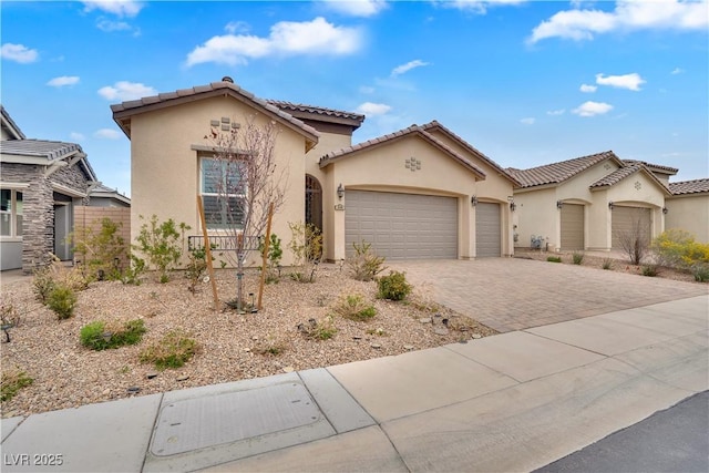 mediterranean / spanish-style house with decorative driveway, a tiled roof, an attached garage, and stucco siding