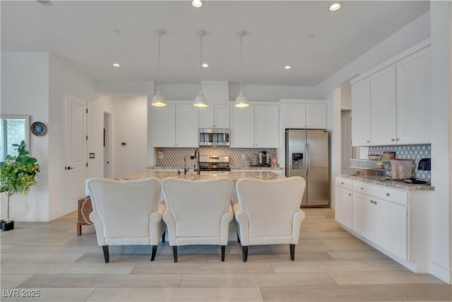 kitchen with light wood-style flooring, stainless steel appliances, white cabinets, a center island with sink, and pendant lighting