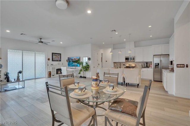 dining space with recessed lighting, a warm lit fireplace, visible vents, and light wood-style flooring