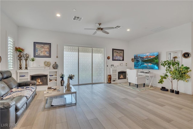 living room featuring a glass covered fireplace, a healthy amount of sunlight, visible vents, and wood finished floors