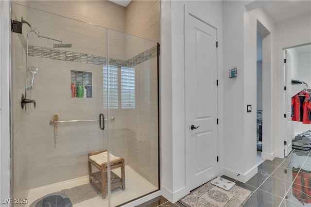 full bathroom with tile patterned floors, a shower stall, a walk in closet, and baseboards