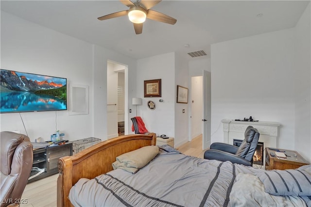 bedroom featuring a ceiling fan, a lit fireplace, visible vents, and light wood-style flooring