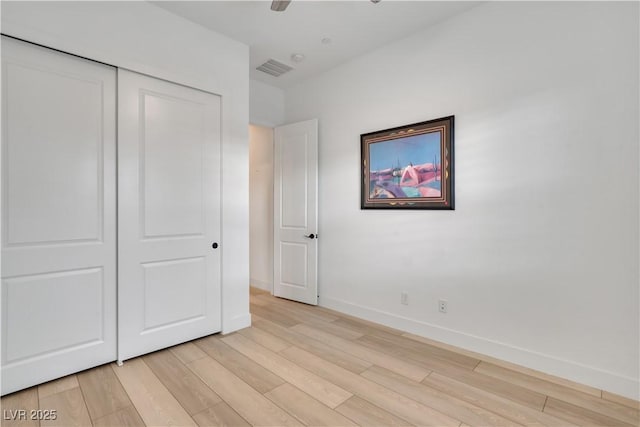 unfurnished bedroom featuring light wood-style flooring, visible vents, a ceiling fan, baseboards, and a closet