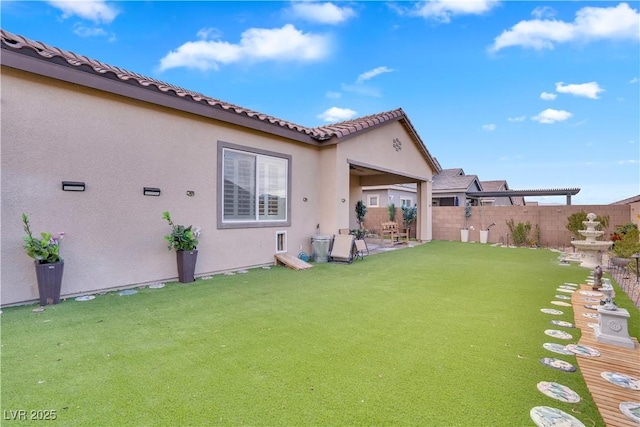 rear view of property featuring a tile roof, fence, a yard, a patio area, and stucco siding