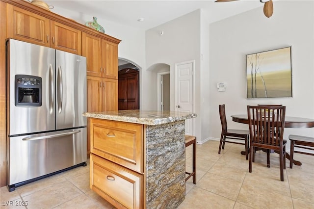 kitchen with light tile patterned flooring, a kitchen island, stainless steel fridge with ice dispenser, light stone countertops, and brown cabinetry