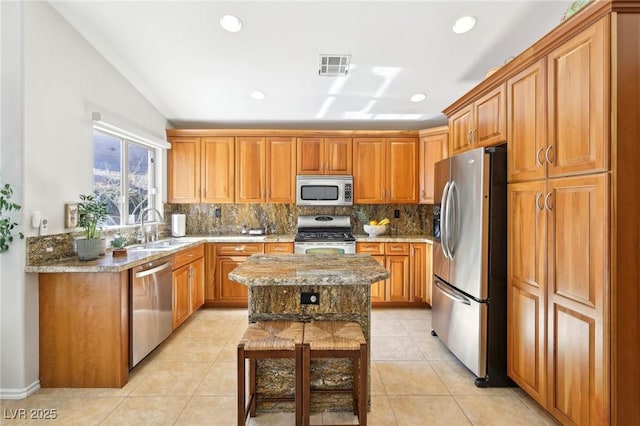 kitchen with light stone countertops, stainless steel appliances, a sink, visible vents, and decorative backsplash