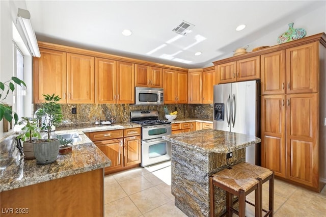 kitchen with brown cabinets, light tile patterned floors, stainless steel appliances, visible vents, and stone countertops