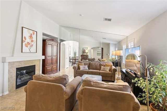 living room featuring arched walkways, light tile patterned floors, a wealth of natural light, visible vents, and a tile fireplace