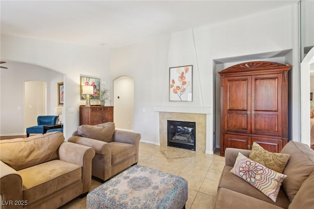 living area with arched walkways, baseboards, light tile patterned flooring, and a tiled fireplace