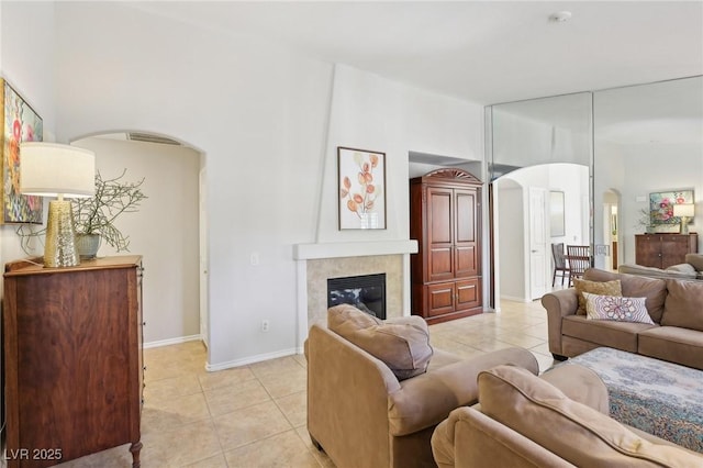 living area with baseboards, a fireplace, arched walkways, and light tile patterned flooring