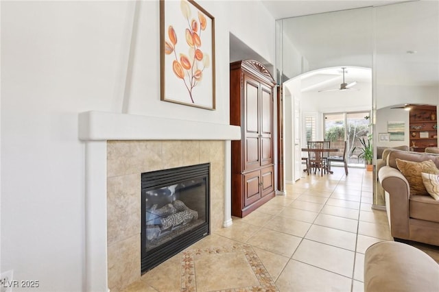 living room featuring a ceiling fan, a tile fireplace, arched walkways, and light tile patterned floors