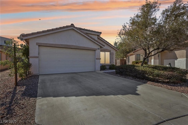 view of front of home featuring an attached garage, driveway, a tiled roof, and stucco siding