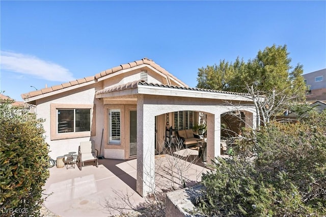 rear view of house featuring a patio area, a tiled roof, and stucco siding