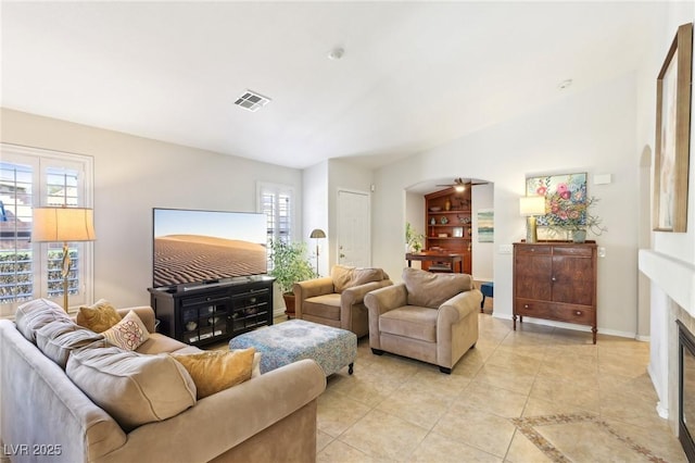 living area with light tile patterned floors, visible vents, a ceiling fan, a glass covered fireplace, and baseboards