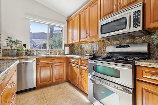 kitchen with stainless steel appliances, light tile patterned flooring, vaulted ceiling, and backsplash