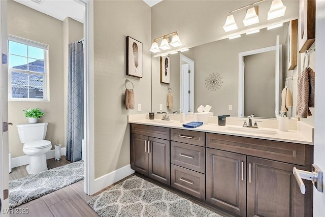 bathroom with toilet, double vanity, baseboards, and a sink