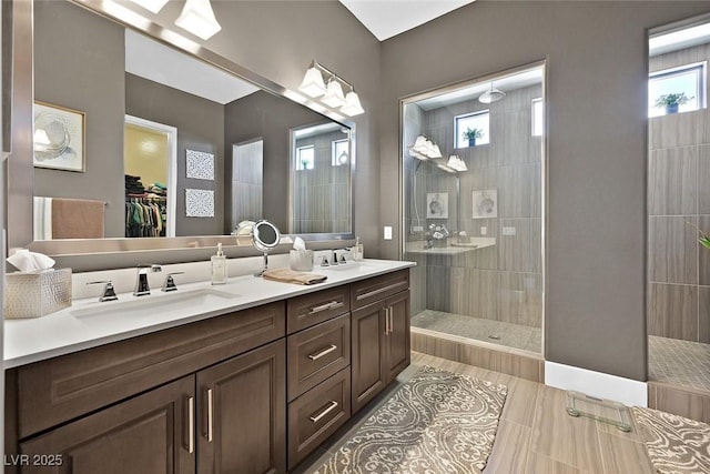 bathroom with double vanity, walk in shower, a sink, and a walk in closet