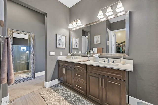 full bath featuring double vanity, a stall shower, baseboards, a spacious closet, and a sink