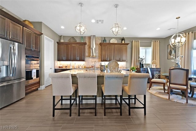 kitchen featuring stainless steel appliances, wall chimney exhaust hood, visible vents, and a kitchen breakfast bar