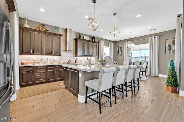 kitchen featuring tasteful backsplash, visible vents, an inviting chandelier, wall chimney range hood, and a kitchen bar