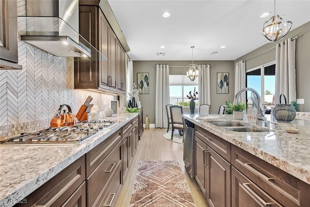 kitchen with wall chimney exhaust hood, appliances with stainless steel finishes, a sink, dark brown cabinets, and a notable chandelier