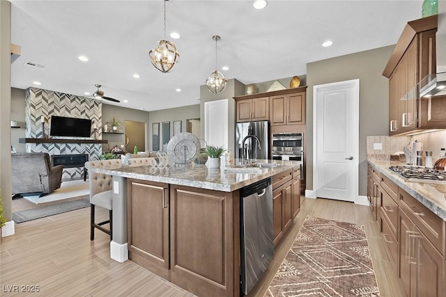 kitchen with stainless steel appliances, a sink, a kitchen breakfast bar, tasteful backsplash, and an island with sink