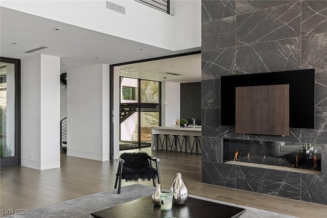 living area featuring a wall of windows, wood finished floors, visible vents, baseboards, and a high end fireplace