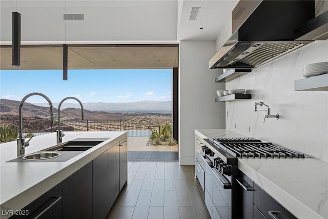 kitchen with visible vents, a sink, dark cabinetry, exhaust hood, and high end range