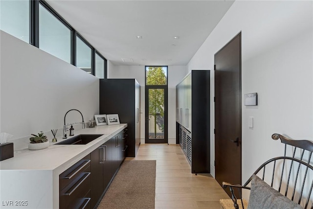 kitchen with floor to ceiling windows, light countertops, light wood-style floors, modern cabinets, and a sink