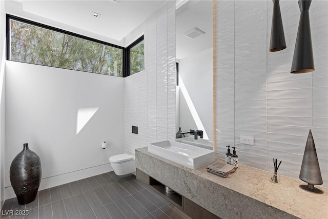 bathroom featuring visible vents, toilet, a sink, tile walls, and tile patterned flooring