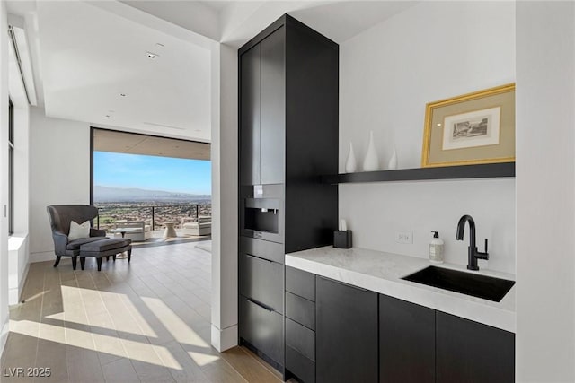 kitchen with a sink, dark cabinets, floor to ceiling windows, and light countertops