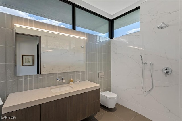 bathroom featuring tile patterned floors, toilet, a marble finish shower, tile walls, and vanity