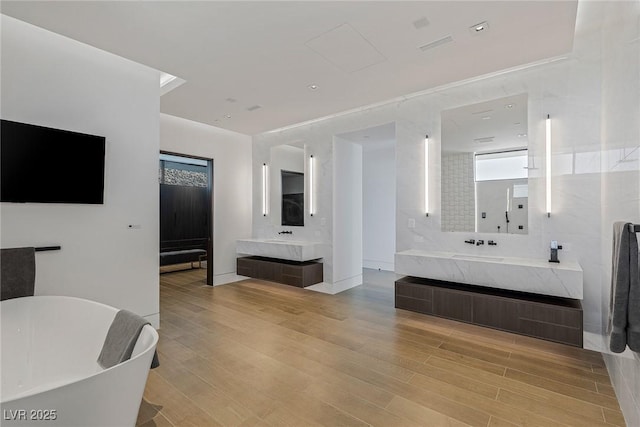 bathroom featuring a sink, a freestanding bath, two vanities, and wood finished floors