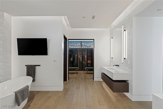 bathroom with a freestanding tub, visible vents, wood finished floors, baseboards, and vanity