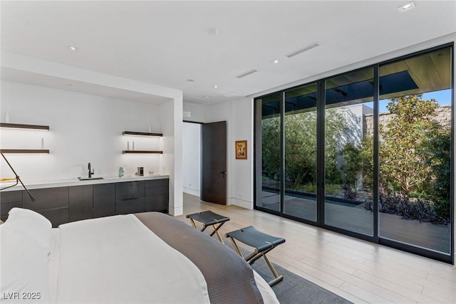 bedroom featuring visible vents, floor to ceiling windows, light wood-style floors, access to outside, and a sink