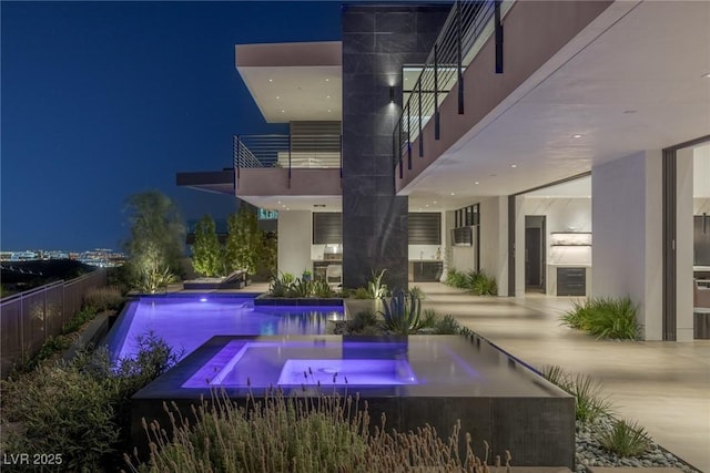 pool at night with an outdoor pool, an in ground hot tub, and a patio