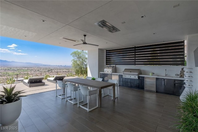 view of patio / terrace with exterior kitchen, a grill, outdoor dining area, a mountain view, and a ceiling fan