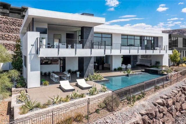 rear view of property featuring a pool with connected hot tub, fence, stucco siding, a balcony, and a patio area