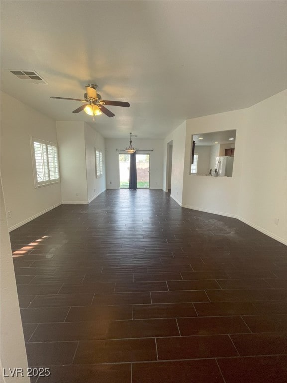 empty room with dark wood-style floors, visible vents, baseboards, and a ceiling fan