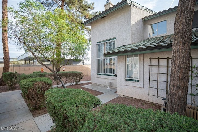 exterior space with a tiled roof, fence, and stucco siding