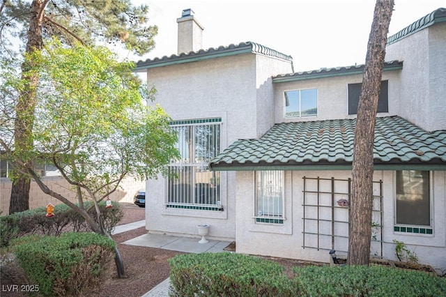 back of property with a chimney, a tile roof, and stucco siding