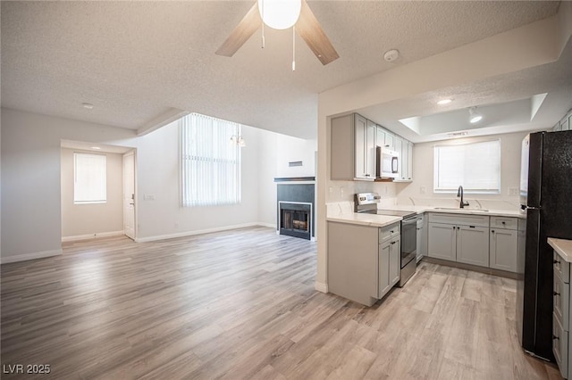 kitchen with white microwave, gray cabinetry, a sink, stainless steel range with electric cooktop, and freestanding refrigerator