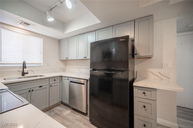 kitchen featuring light stone counters, light wood-style flooring, freestanding refrigerator, a sink, and dishwasher