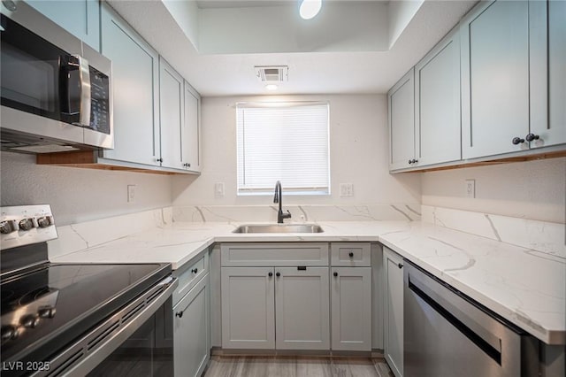 kitchen with light stone counters, stainless steel appliances, a sink, visible vents, and gray cabinets