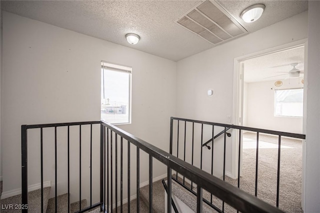 corridor featuring a textured ceiling, carpet floors, visible vents, an upstairs landing, and baseboards